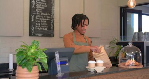 Smiling african american barista packing takeaway coffee and pastry at cozy cafe counter