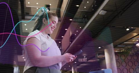 Young woman tapping smartphone creating augmented waveform overlay in modern atrium