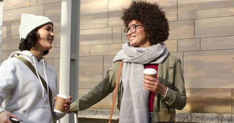 Urban friends sharing coffee and conversation on sidewalk, smiling, casual winter fashion