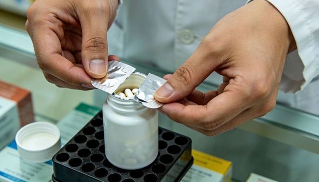 Pharmacist hands dispensing capsules into prescription bottle from blister pack at counter