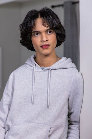 Contemplative asian teen leaning on wall wearing gray hoodie and chain indoor portrait