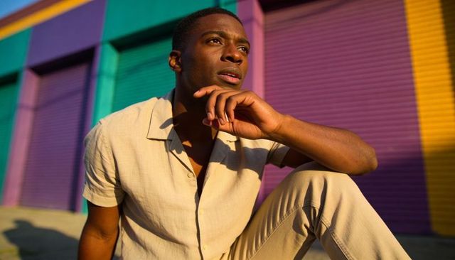 Young man crouching in beige outfit against vibrant colorblock shutters at golden hour
