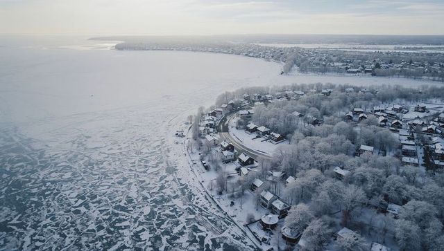 Aerial winter coastline: snow-covered peninsula curving into frozen bay with ice floes