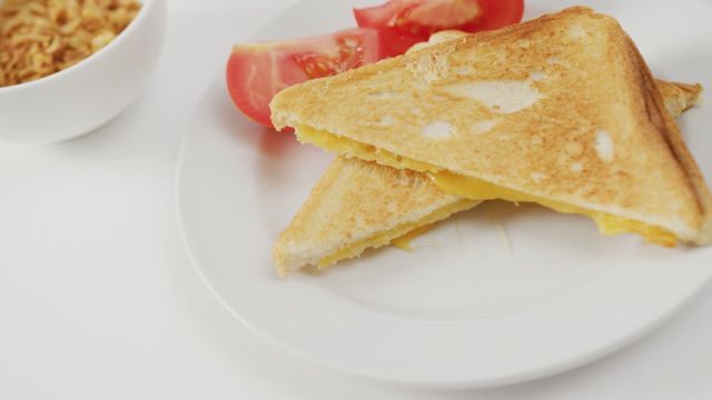 Freshly prepared cheese sandwich on white bread served with sliced tomatoes, offering a tasty combination of melting cheese inside toasted slices. Ideal for illustrating breakfast meals, quick snack ideas, or fusion food visuals. Perfect for food blogs, recipe websites, and advertisements focusing on easy home-cooked meals.