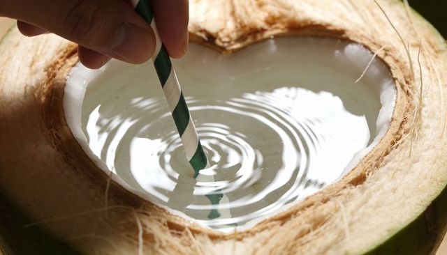 Hand placing green-striped paper straw into heart-shaped opened coconut creating ripples