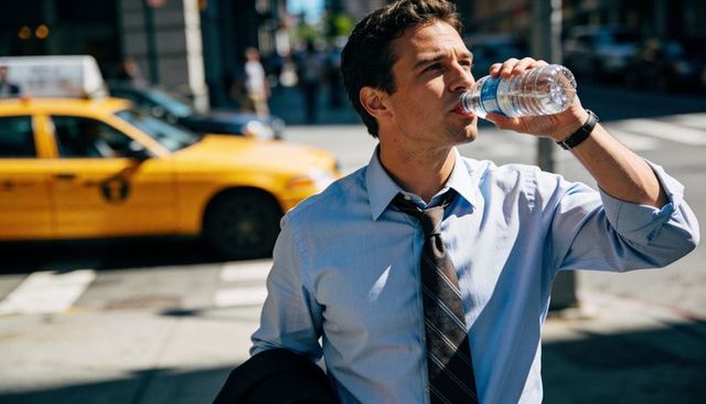 Businessman drinking water at sunny city crosswalk with yellow taxi