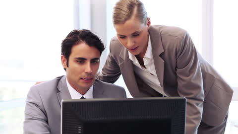 Focused Colleagues Discussing Work Over Computer in Office Setting