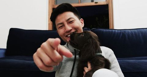 Smiling man with puppy pointing at camera in cozy living room