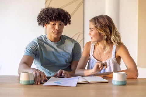Young couple reviewing budget and documents at wooden table with notebook and cups