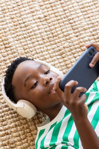 African american boy listening to music on smartphone while lying on woven rug