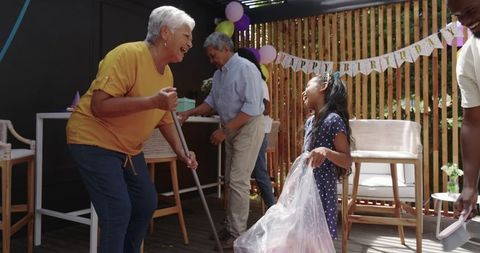 Multigenerational Family Celebrating Birthday on Sunlit Backyard Deck Laughing Together