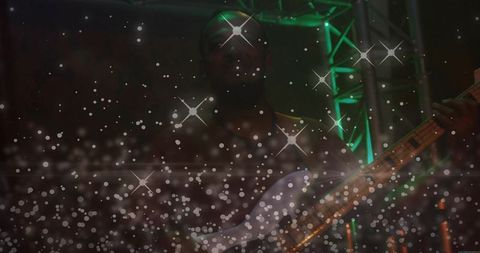 Silhouetted bassist playing live on stage with green rig lighting and sparkling bokeh flares