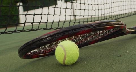 Tennis ball and racket resting on outdoor hard court near taut net for training and play