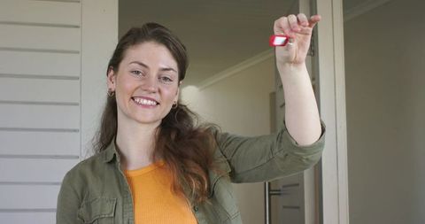 Smiling woman holding new house key on red fob in doorway celebrating homeownership
