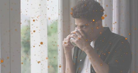 Man sipping coffee by window through sunlit dust film, contemplative morning ritual
