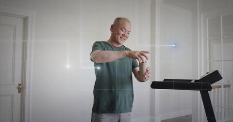 Asian man holding travel cup by treadmill in modern home smiling and preparing drink