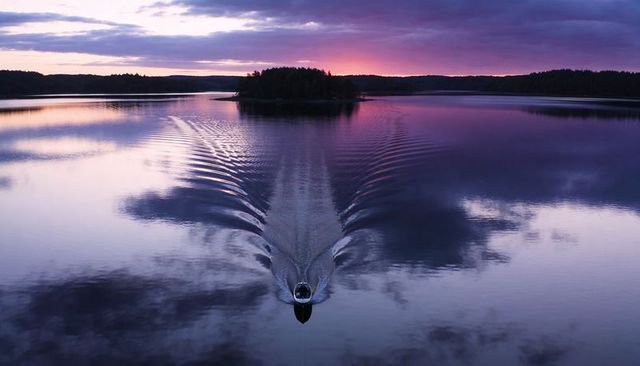 Motorboat gliding across glassy lake leaving v-shaped wake at purple twilight