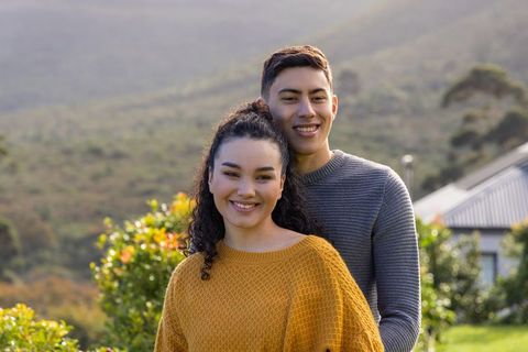 Young couple embracing in backyard garden on hillside wearing mustard sweater and gray knit