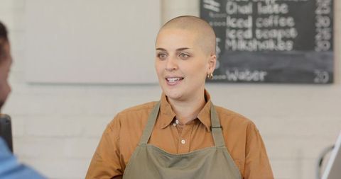 Friendly shaved-head barista serving african american customer at coffee counter