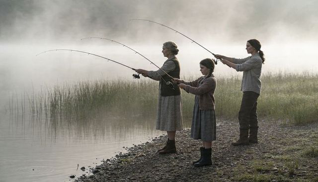 Three generations fishing on misty lakeshore casting lines at dawn for quiet family moment