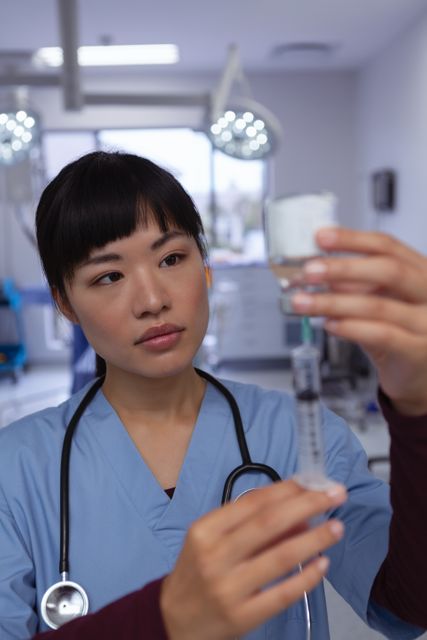 Depicts a female surgeon carefully filling a syringe with medicine from an ampule in a hospital operating room. The image is suitable for use in healthcare-related content, education materials, medical training resources, and articles focusing on medical procedures and healthcare workers.
