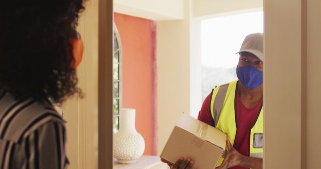 Delivery worker wearing facemask and gloves handing parcel to customer at her doorstep, exemplifying contactless delivery. Ideal for illustrating safe delivery services during pandemic, customer satisfaction, home delivery, and logistics.