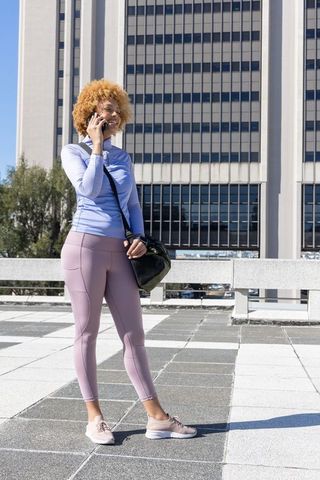 African american woman talking on smartphone in activewear on urban rooftop plaza
