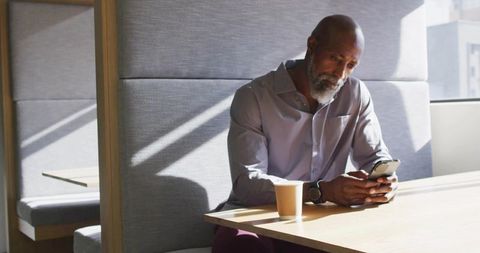 Senior man relaxing at cafe table with smartphone