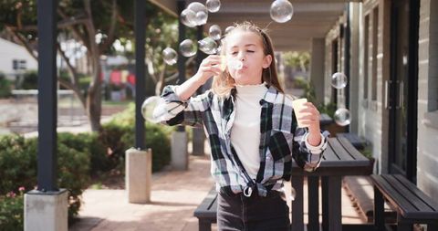 Young Girl Joyfully Blowing Soap Bubbles Outdoors in Sunny Courtyard