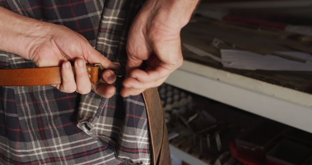 Hands Tightening Brown Leather Belt on Plaid Shirt in Rustic Workshop - Download Free Stock Images Pikwizard.com