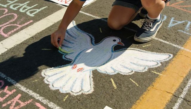 Kneeling teen drawing colorful chalk dove on asphalt street grid during community art fair