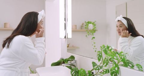 Asian Woman Practicing Skincare Routine in Minimalist Bathroom