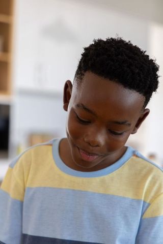 African american preteen boy smiling while looking down in pastel striped tee, soft natural light