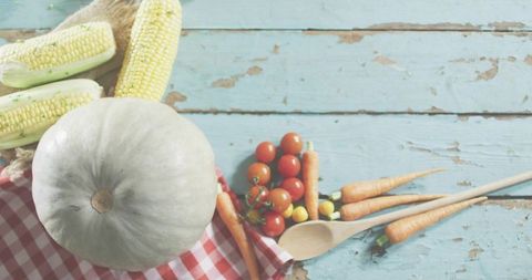 Rustic fall harvest featuring white pumpkin, corn, cherry tomatoes and baby carrots