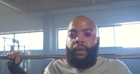 Bearded athlete performing barbell squat showing strength sweat and determination