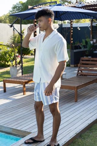 Young african american man standing by pool on wooden deck wearing striped swim shorts