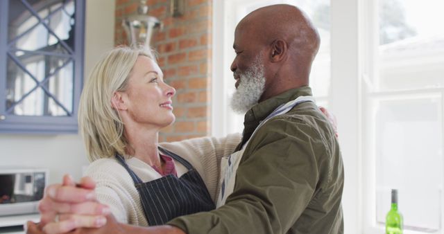 Biracial senior couple wearing aprons dancing together in the kitchen at home. retirement senior couple lifestyle living concept