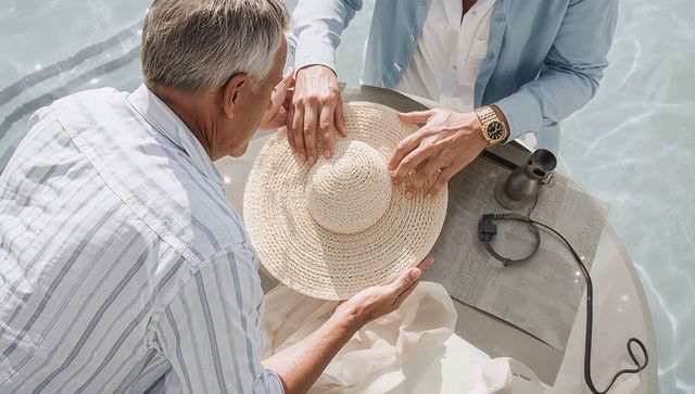 Couple adjusting straw hat at poolside table, summer leisure and gentle companionship