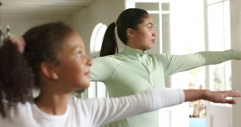 Mom and daughter stretching at home near sunlit french doors for family fitness