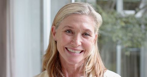 Elegant Senior Woman Smiling by Window in Natural Light with Blouse