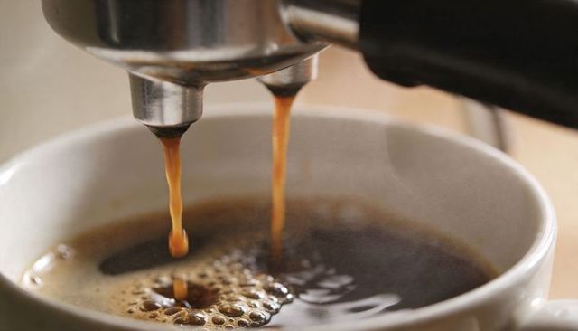 Pulling espresso shot from portafilter into white cup with rich crema closeup
