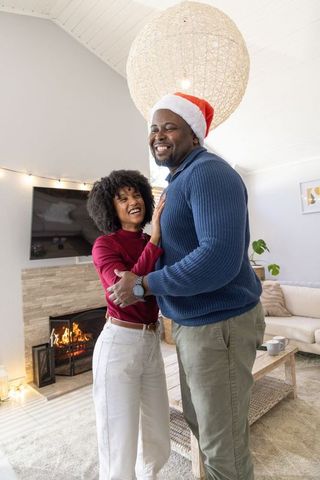 African American Couple Embracing and Laughing by Fireplace Wearing Santa Hat