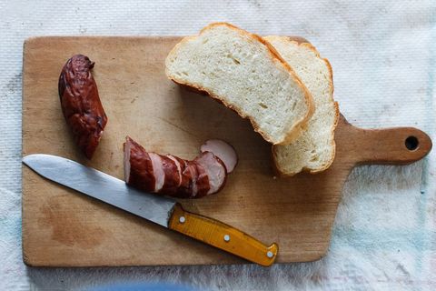 Slicing smoked sausage with bread on wooden cutting board