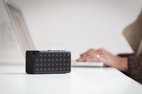 Compact bluetooth speaker streaming sound while person typing on laptop
