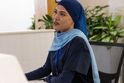 Confident muslim woman in navy hijab collaborating at modern office desk with lanyard