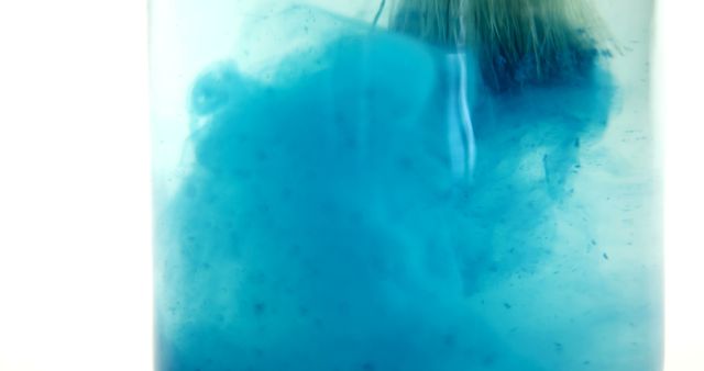 A close-up view of a blue substance dissolving in water, with copy space. The image captures the moment of a chemical reaction or a mixing process, creating an abstract and artistic effect.