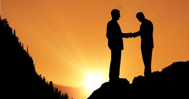 Silhouette of two businessmen shaking hands during sunset, symbolizing partnership, agreement, and successful collaboration. Ideal for use in business presentations, websites, and promotional materials to convey themes of teamwork, cooperation, and professional success.