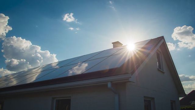 Solar panels on house roof with sunburst in blue sky