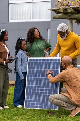 African american family installing solar panel in backyard under pergola during autumn