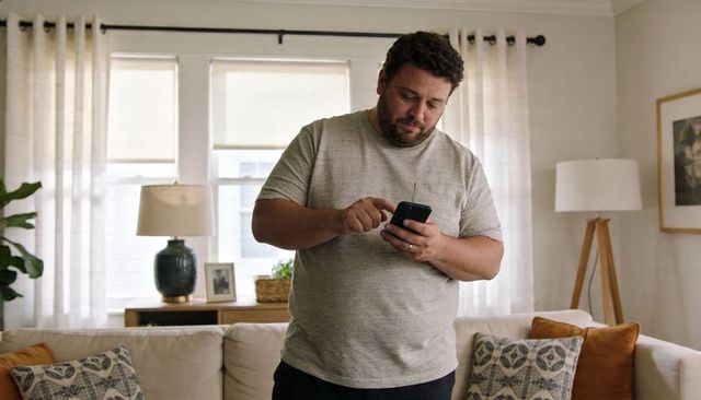 Man using smartphone in cozy sunlit living room with neutral sofa and lamps